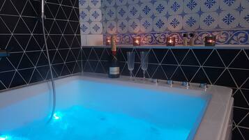 A bathtub with a blue light, a bottle of Moet & Chandon champagne, and candles on a shelf.