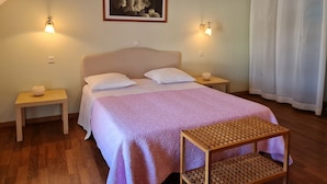 A bedroom with a bed, two bedside tables, a small wooden bench, a wall-mounted picture, and a window with white curtains.