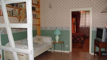 A room with a bunk bed, a small table with a lamp, a television, and a bookshelf.