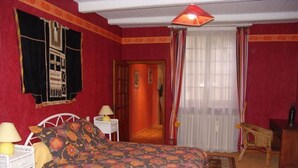 A bedroom with a bed, a nightstand, a lamp, a chair, and a window with curtains. - Charming Accessible Yemeni Suite in the Heart of Argonne (Futeau)