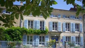 Ein zweistöckiges Gebäude mit blauen Fensterläden, einem Blumenbeet und einem weißen Zaun.