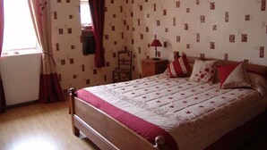 A bedroom with a bed, a nightstand, a chair, a window with curtains, and patterned wallpaper. - Stay in the heart of Joan of Arc's land with 4 unique rooms (Montigny-lès-Vaucouleurs)