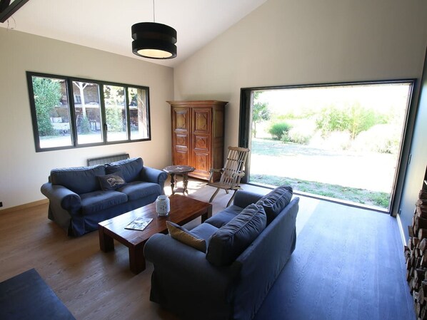 Ein großzügiger Wohnraum mit zwei Sofas, einem Couchtisch und einer Holzkabine. Große Fenster bieten Blick ins Freie.