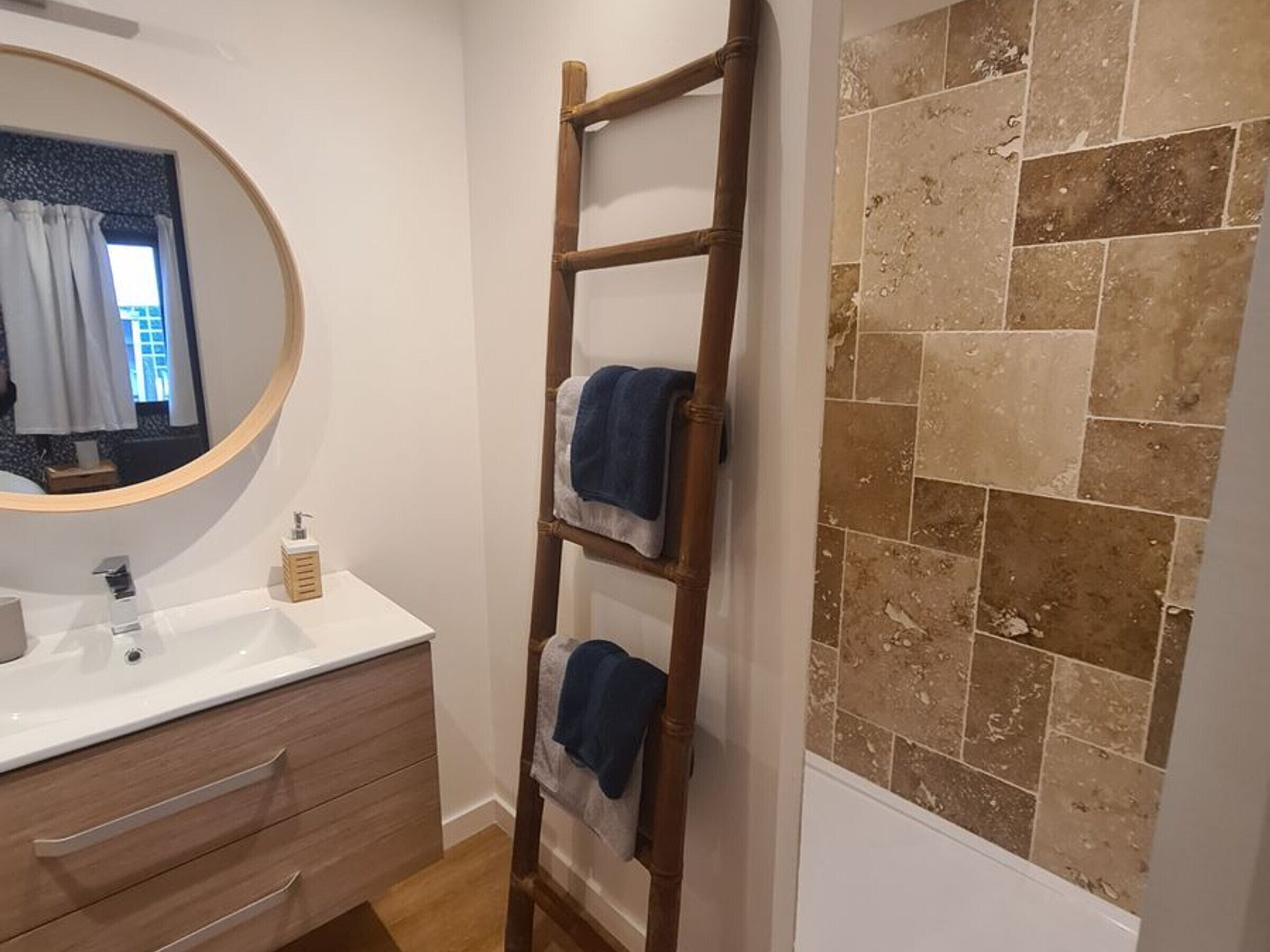 A bathroom with a wooden ladder, a round mirror, a white sink, and a tiled wall.