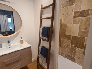 Ein Badezimmer mit einer Holzleiter, einem runden Spiegel, einem weißen Waschbecken und einer gefliesten Wand.