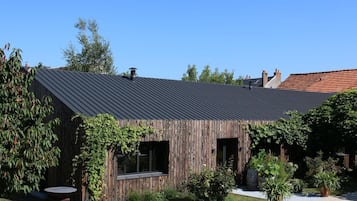 A rustic wooden building with a metal roof, surrounded by greenery and a gravel path.