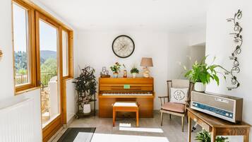Una habitación con un piano, una silla, una mesa con una radio y una planta en maceta.