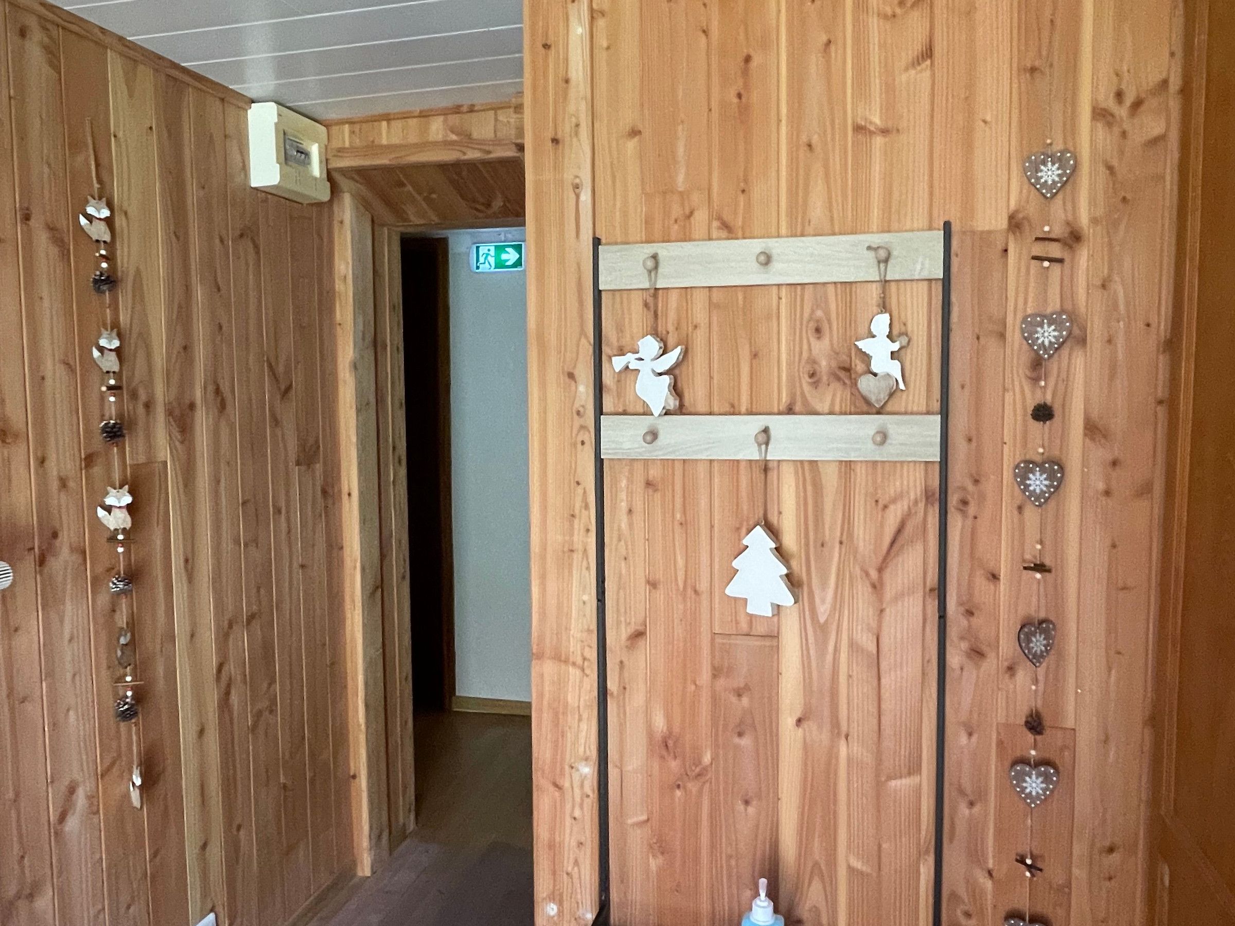 Een houten hal met een houten deur, een wandplank met decoratieve objecten en een bord met richtingaanwijzingen.
