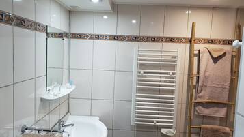 Baño con lavamanos blanco, espejo y perchero. Zona de ducha con escalera de madera y otro perchero.