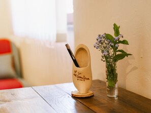En træpenneholder med en pen på en underkop, ved siden af en glasvas med blomster på et træbord.