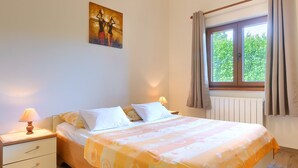 Un dormitorio con cama, mesitas de noche, una ventana con cortinas y un cuadro en la pared.