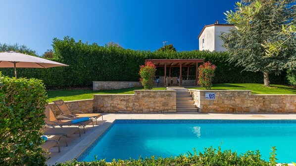 A swimming pool with lounge chairs, a pergola, and a stone wall.