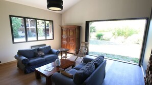 Amplia sala de estar con dos sofás, una mesa de centro y un mueble de madera. Amplias ventanas ofrecen vistas al exterior.