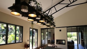 Un comedor moderno con una mesa larga, varias sillas, luces colgantes y ventanas amplias que dan a zonas verdes.