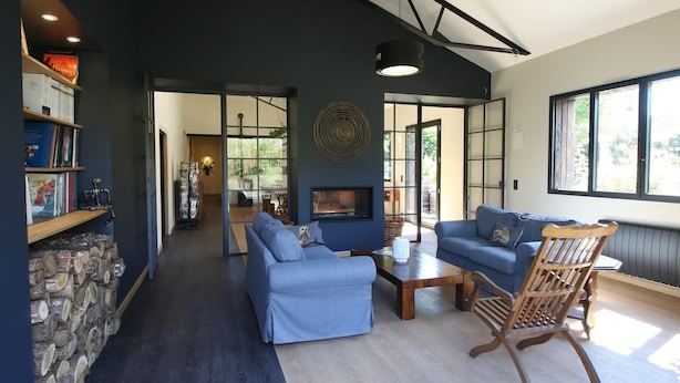 Una sala de estar moderna con chimenea, sofás azules, una silla de madera y una estantería.