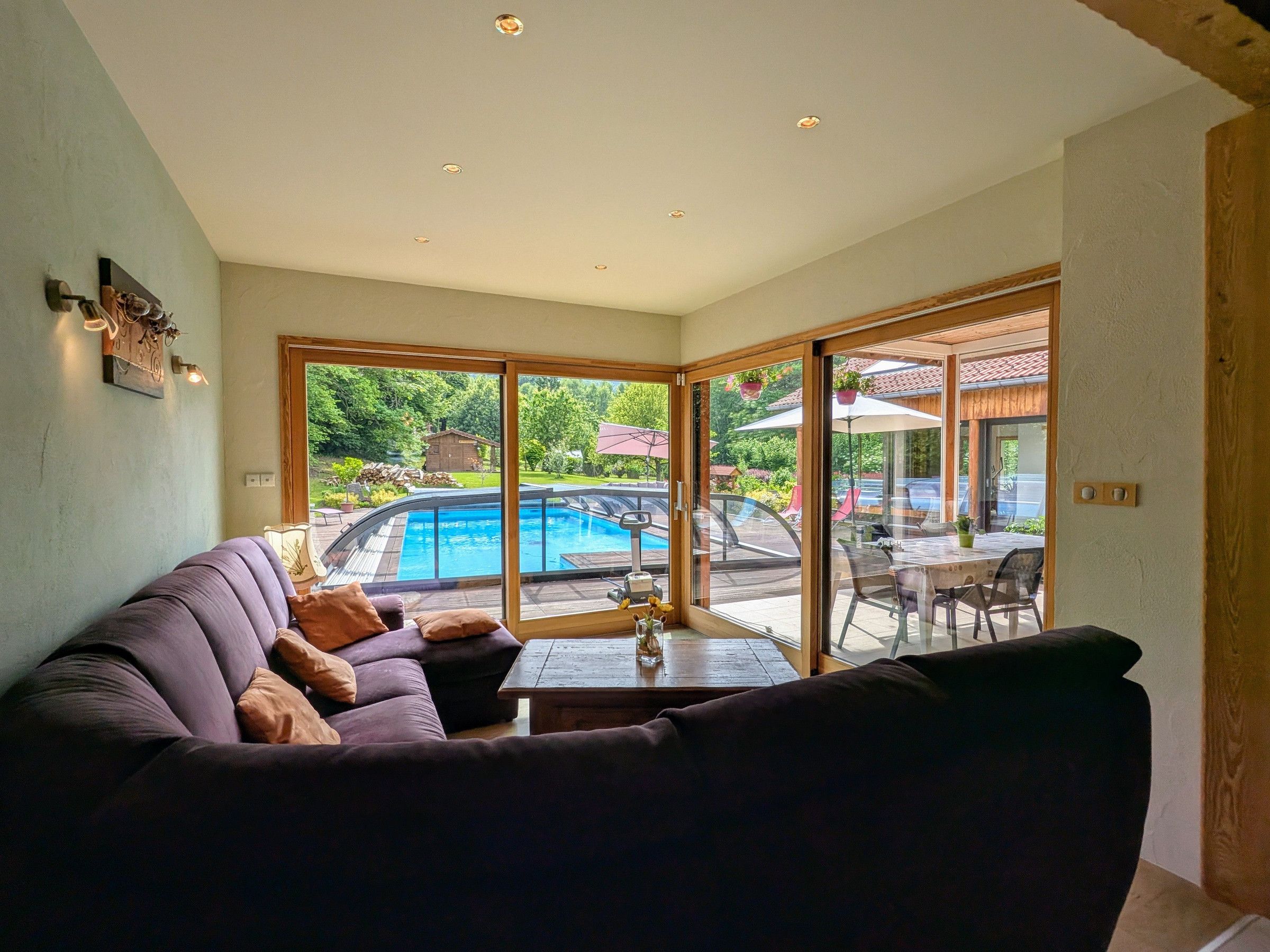A living room with a sofa, a coffee table, and a view of a swimming pool through large glass doors.