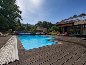 A swimming pool with a wooden deck, lounge chairs, and a glass-enclosed area. - Family room with pool and SPA in Anould (Anould)