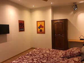 Une chambre à coucher comprenant un lit, une armoire en bois, un téléviseur à écran plat fixé au mur et deux affiches accrochées au mur.