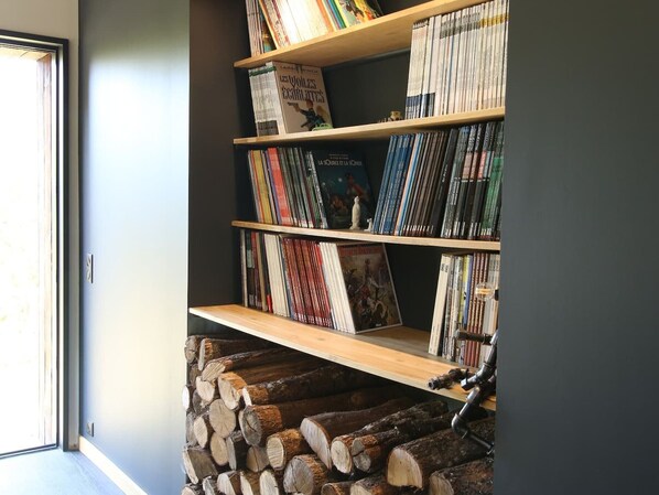 Une bibliothèque remplie de livres et de DVD, une étagère en bois et une pile de bois de chauffage.