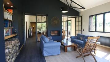 Un salon moderne avec une cheminée, des canapés bleus, un fauteuil en bois et une bibliothèque.