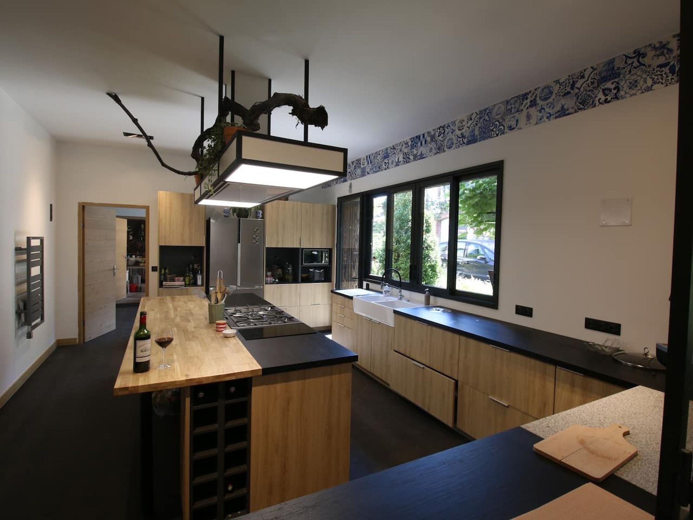 Una cocina moderna con una isla central, armarios de madera, un refrigerador de acero inoxidable y un amplio ventanal con vistas al exterior.