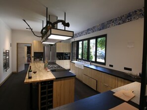 Eine moderne Küche mit Kochinsel, Holzschränken, einem Edelstahlkühlschrank und einem großen Fenster mit Blick ins Freie.
