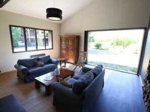 Ein großzügiger Wohnraum mit zwei Sofas, einem Couchtisch und einer Holzkabine. Große Fenster bieten Blick ins Freie.