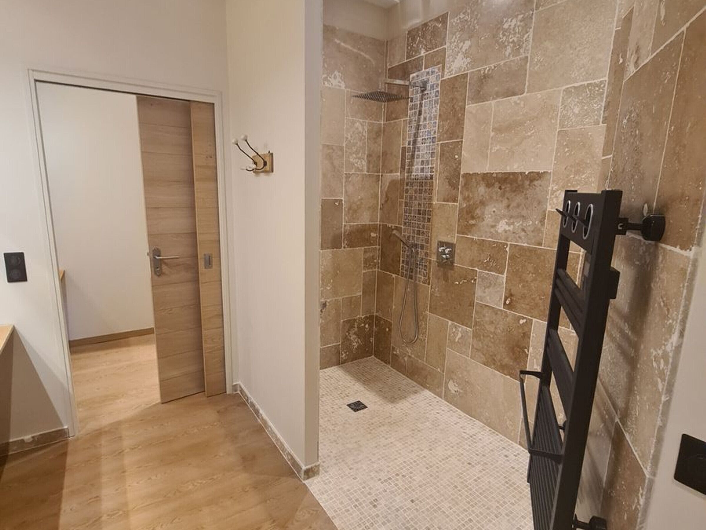 Zona de ducha con paredes de azulejos y suelo de madera.