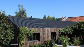 Ein rustikales Holzgebäude mit Metalldach, umgeben von Grün und einem Kiesweg.
