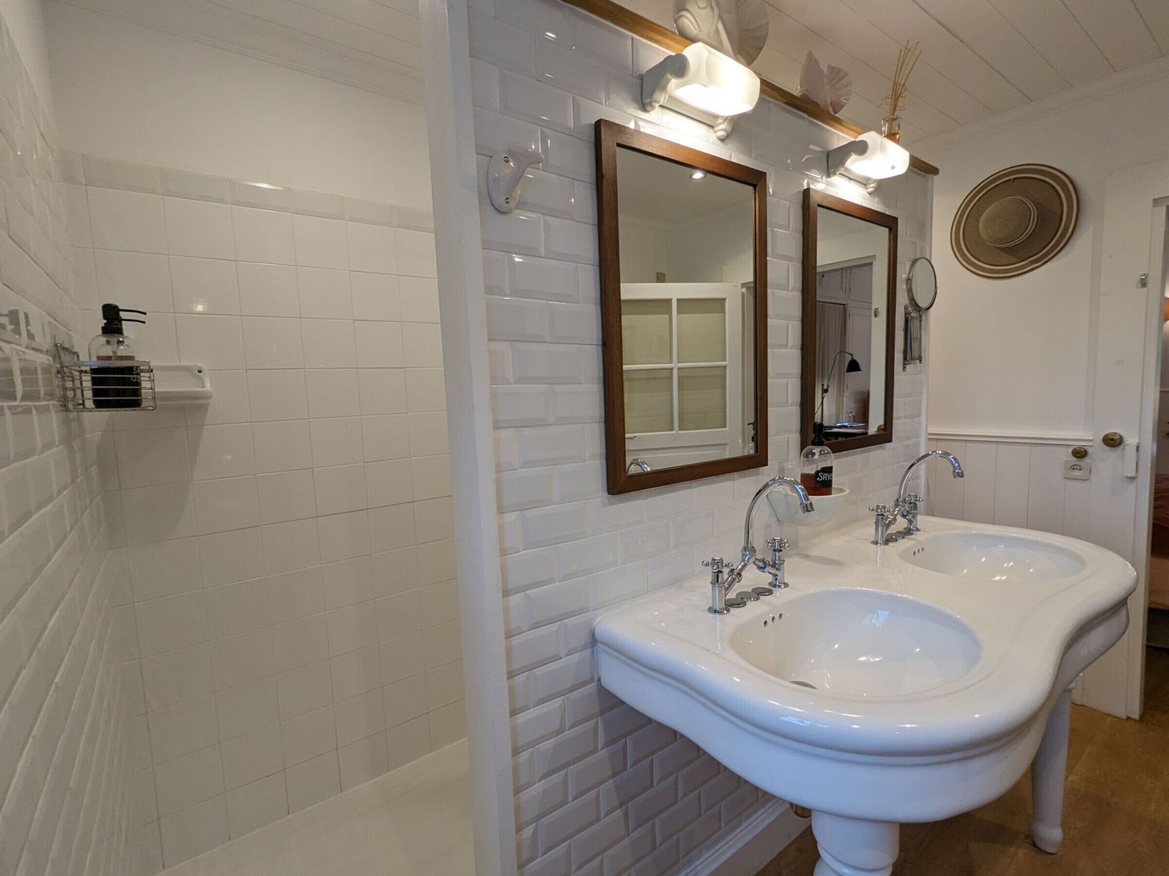 Een badkamer met witte betegelde muren, twee wastafels en twee spiegels met houten lijst.