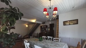 En matplats med ett bord täckt av en mönstrad duk, omgivet av vita stolar. En kristallkrona med röda lampskärmar hänger ovanför bordet.