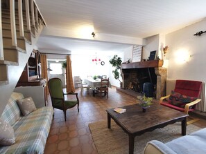 A cozy living room with a fireplace, a dining area, and a staircase leading to an upper floor.