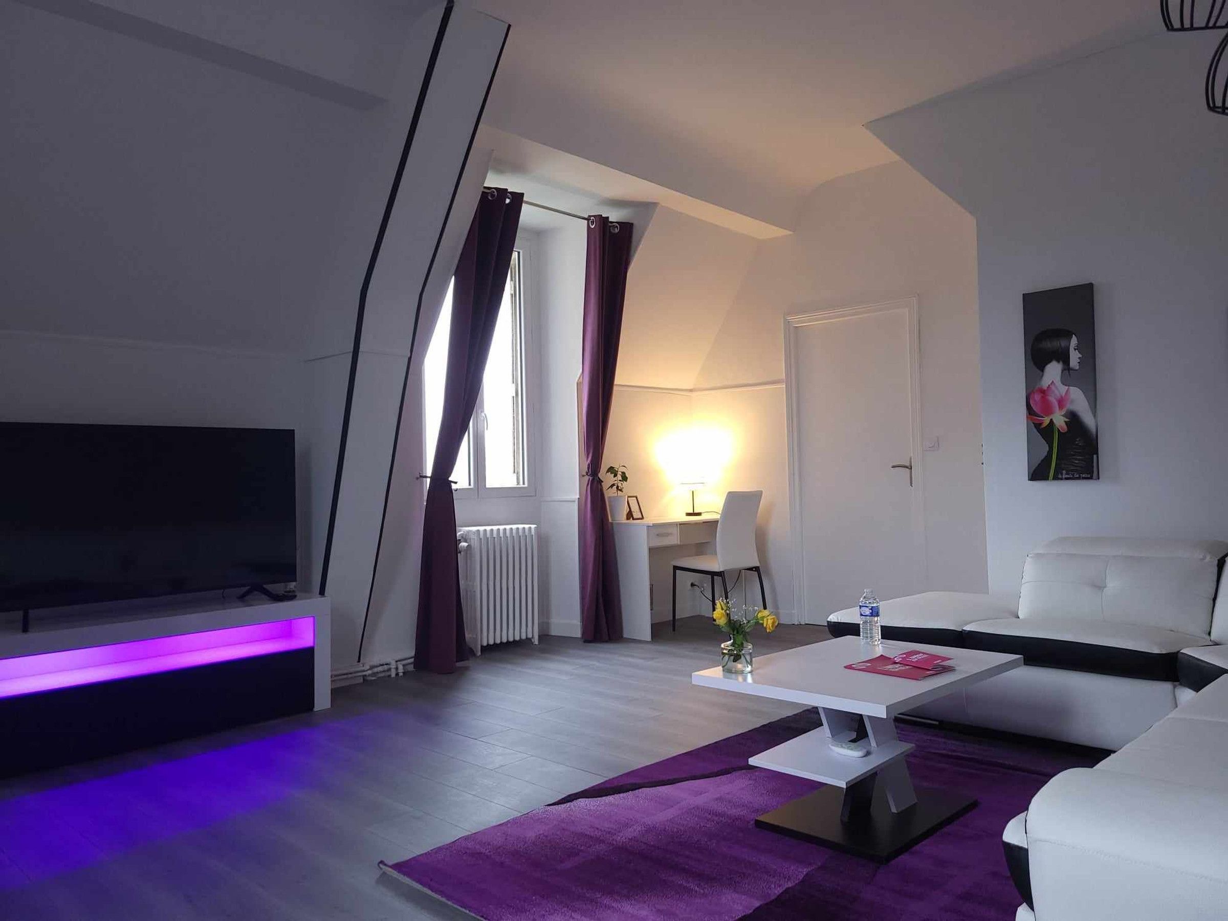 Un salon moderne avec un téléviseur à écran plat, un canapé blanc, une table basse et un tapis violet.