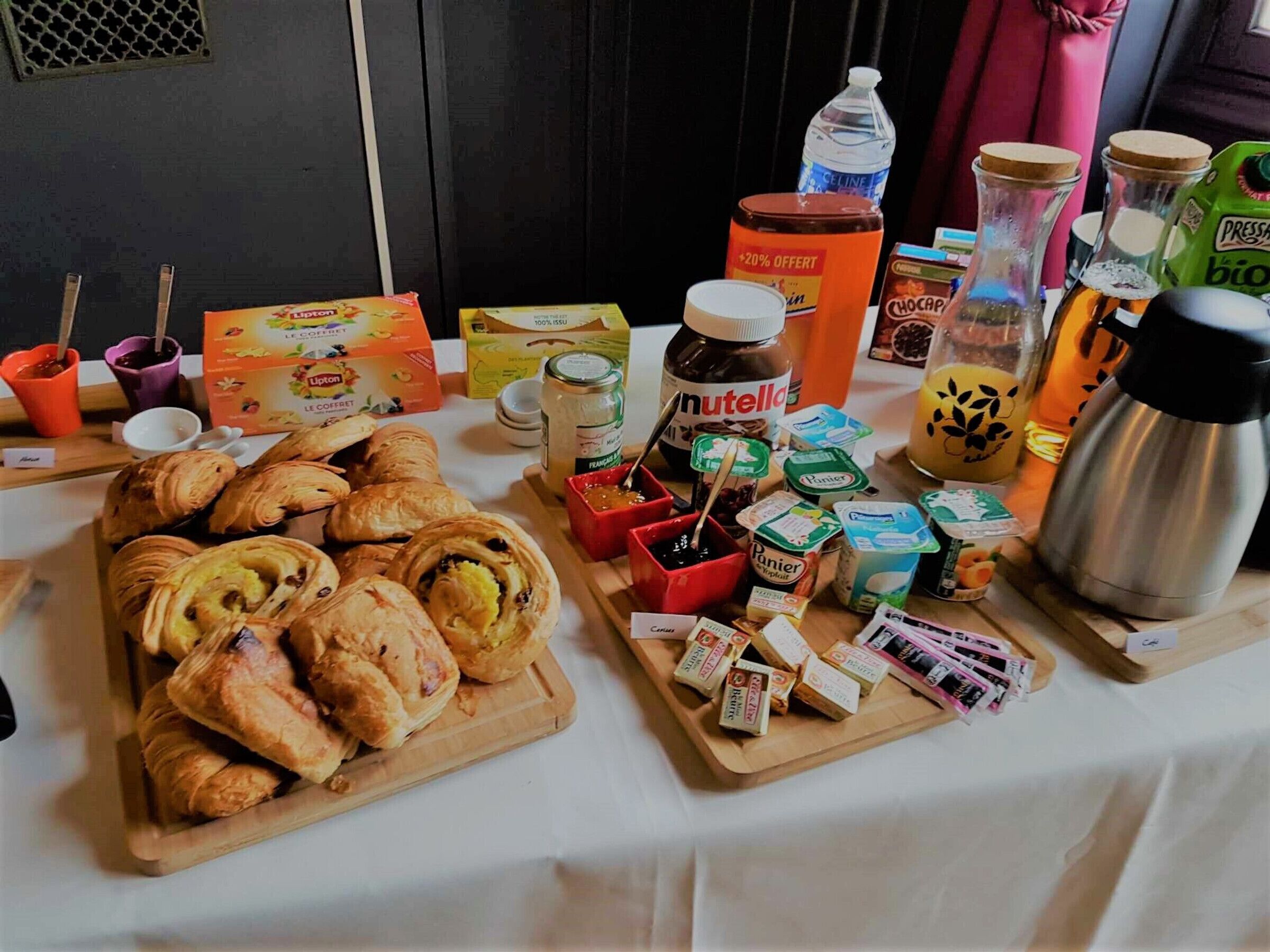 Un buffet de petit-déjeuner avec des viennoiseries, du Nutella et diverses confitures sur une table.