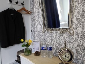A hotel room with a mirror, a clock, a vase with flowers, a water bottle, and a black jacket hanging on a rack. - Elegant stay at Château, modern comfort and nearby activities (Cluis)