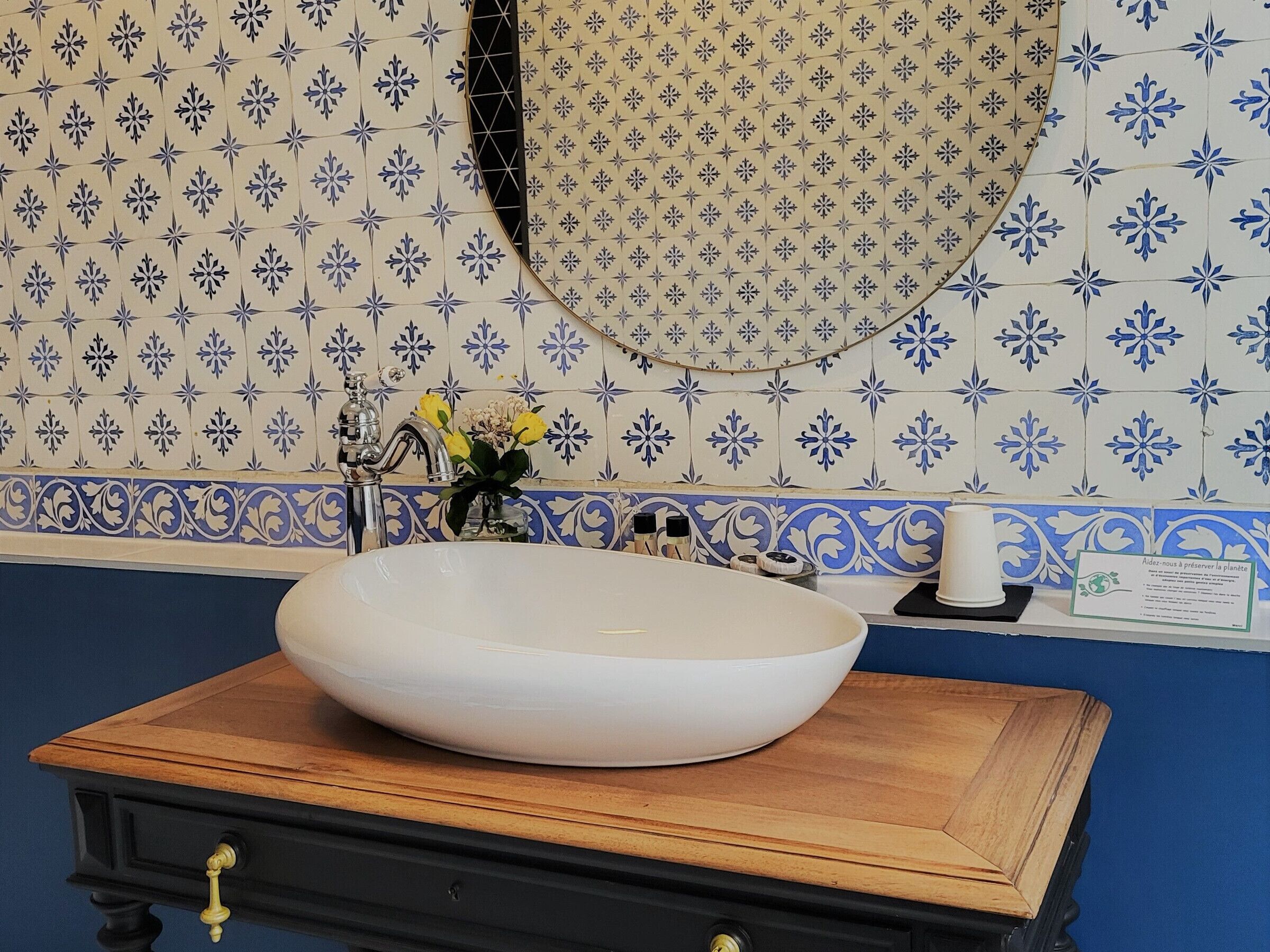 A bathroom with a white sink, blue and white patterned tiles, a mirror, and a wooden vanity.