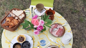 A picnic setup with bread, pastries, flowers, and various dishes on a table outdoors.