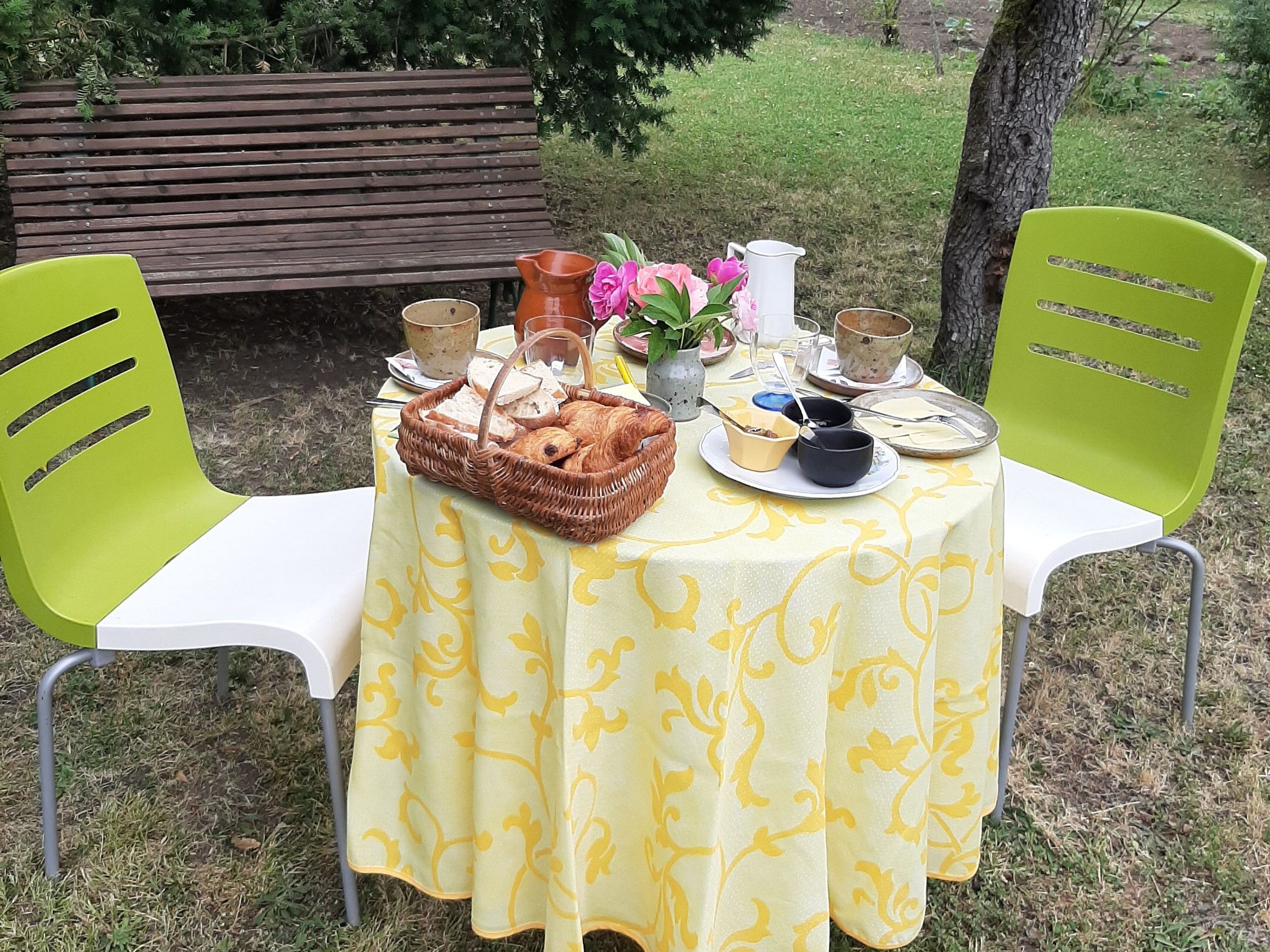Ein Essbereich im Freien mit einem Tisch, der mit einer gelben Tischdecke bedeckt ist, umgeben von grünen Stühlen.