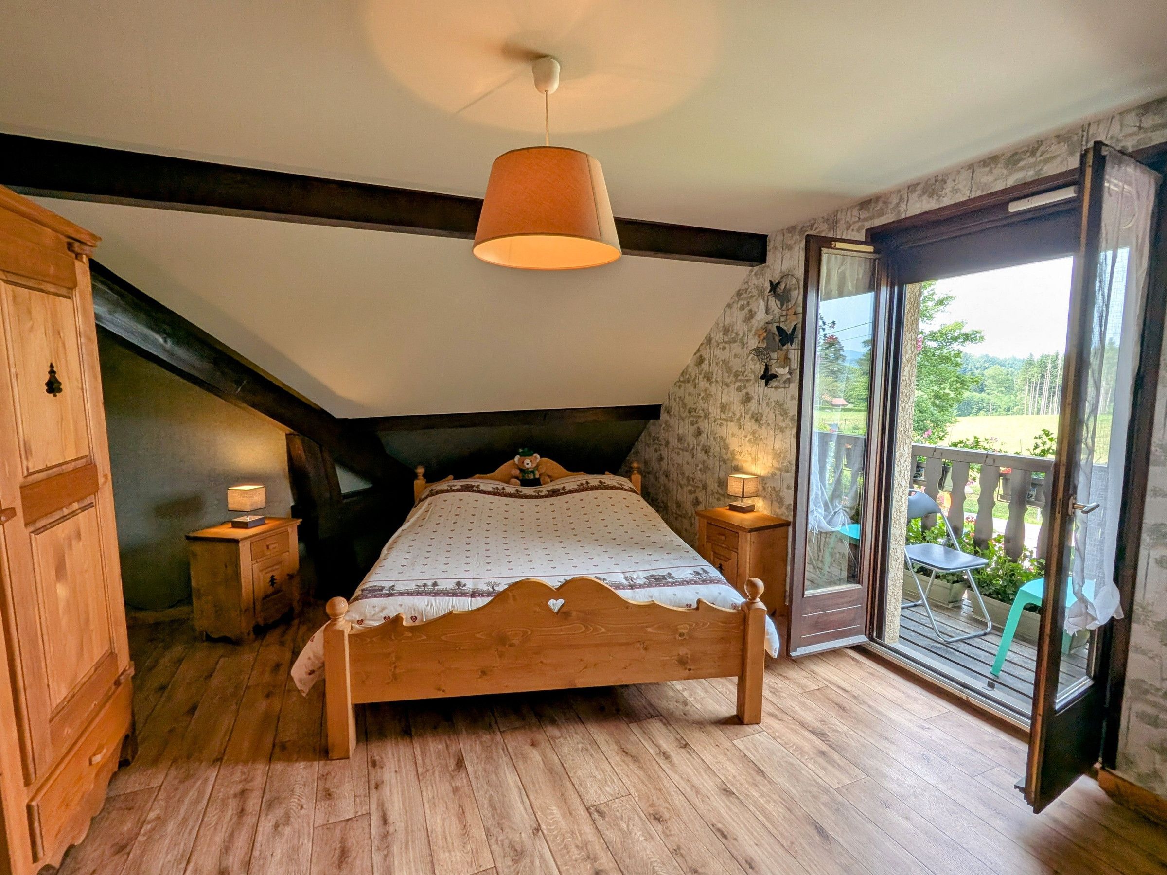Quarto com cama de madeira, teto inclinado e grande porta de vidro deslizante que dá para uma varanda.