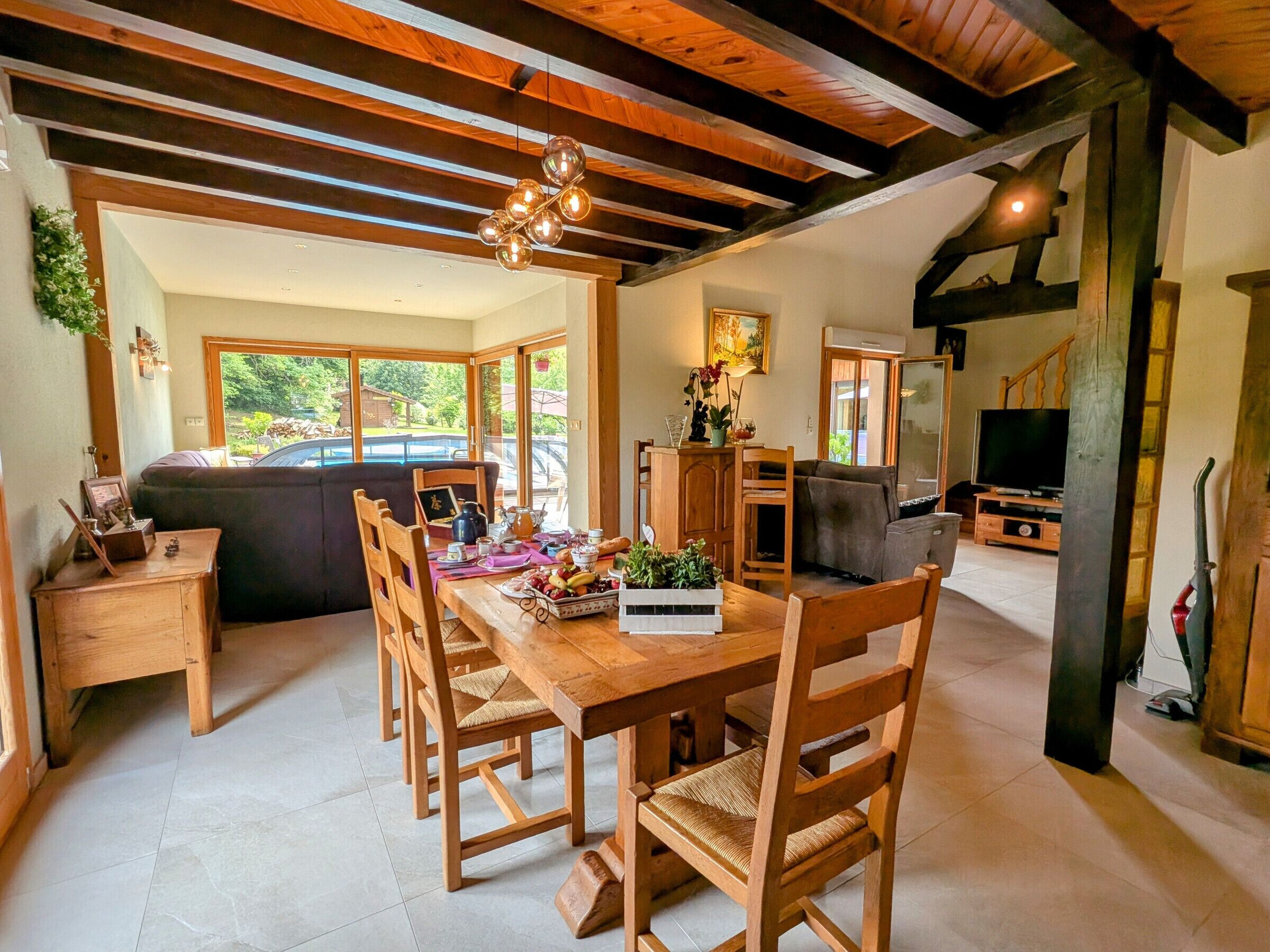 Un coin repas avec une table et des chaises en bois, un canapé et un téléviseur en arrière-plan.