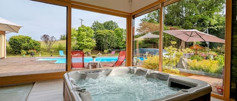 A hot tub with a view of a swimming pool and garden.