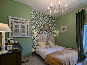 A bedroom with a bed, a dresser, a chandelier, and a wall with a leafy wallpaper pattern. - Renovated guest house with dining in Altiligerian countryside (Saint-Victor-sur-Arlanc)