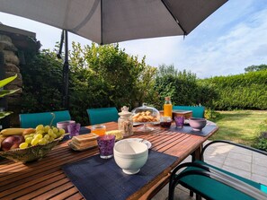 Een buitenontbijtplaats met een gedekte tafel, inclusief fruit, brood en drankjes.