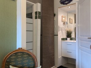 Een hotelkamer met een groene fauteuil met patroon, een witte kast, en een badkamer met een spiegel en prestatiebeelden.
