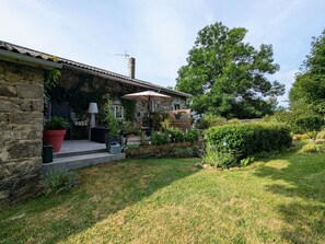 A stone house with a covered porch, potted plants, and a well-maintained lawn. - Renovated guest house with dining in Altiligerian countryside (Saint-Victor-sur-Arlanc)