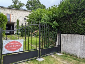 Une entrée fermée par un portail mène à la propriété appelée « Chambre d'Hôtes Le Clos de l'Arzon », avec un bâtiment en pierre et une végétation luxuriante en arrière-plan.