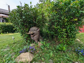 Een tuin met een standbeeld van een leeuw, omringd door begroeiing en rotsen.