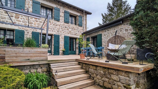 Un bâtiment en pierre doté d’une terrasse en bois, d’un espace salon extérieur et d’un fauteuil suspendu.