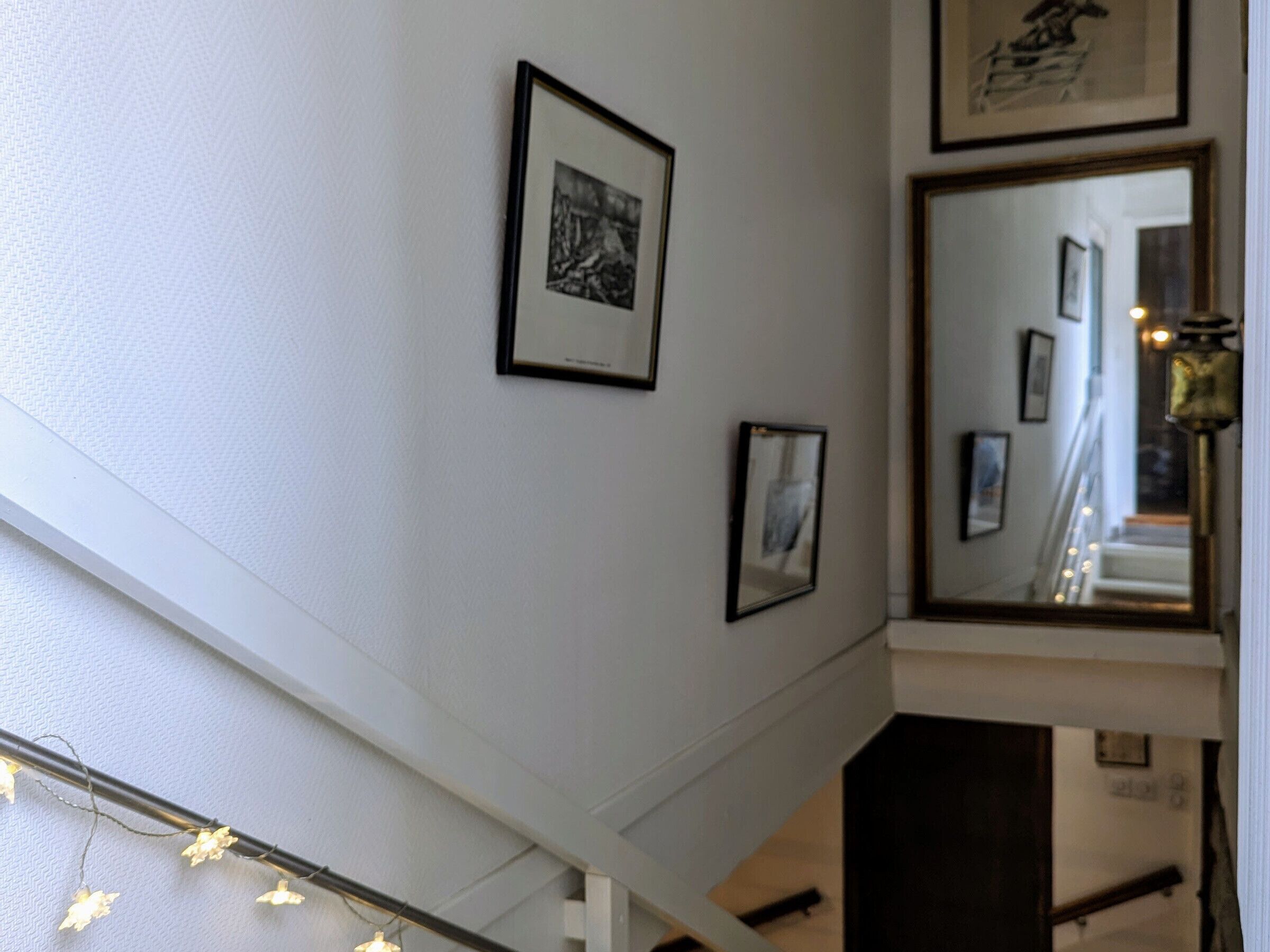 A staircase with a white wall, a framed picture, and a mirror reflecting part of the room.