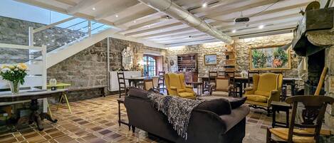 Un amplio salón con techo alto, paredes de piedra y una zona de comedor con mobiliario de madera.